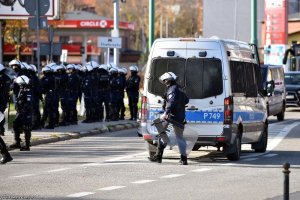 Policjanci w kamizelkach i hełmach podczas zabezpieczenia meczu, widoczny policyjny radiowóz.