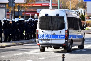 policyjny radiowóz, w tle policjanci zabezpieczający mecz piłki nożnej.