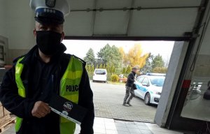 Policjant trzyma ulotkę, za nim widoczny mężczyzna i radiowóz.