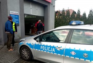 Radiowóz, policjant i osoby przed stacją diagnostyczną.