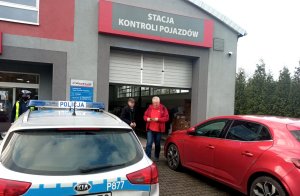 Radiowóz, policjant i osoby samochód przed stacją diagnostyczną.