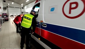 Diagnosta sprawdza światła w karetce obok policjant.