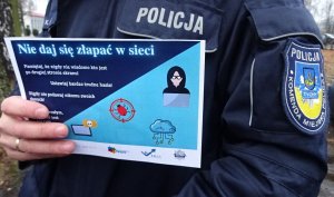 Umundurowany policjant trzyma ulotkę zatytułowaną &quot;Nie daj się złapać w sieci&quot;.