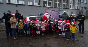 Zdjęcie grupowe dzieci w czerwonych czapeczkach, pani, mikołaja, policjantów i strażników miejskich.