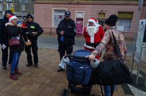 Kobieta robi zdjęcie obok stoją policjanci I Mikołaj, rozmawiają z kobietą z dzieckiem w wózku.