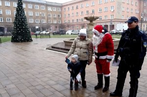 Kobieta z dzieckiem, Mikołaj i dzielnicowy, po lewej stronie choinka.