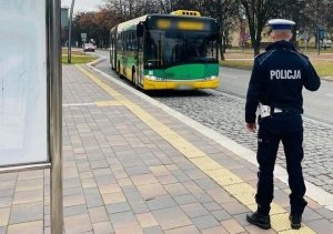 Umundurowany policjant na przystanku autobusowym, widoczny dojeżdżający autobus.