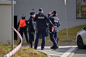 Umundurowani policjanci rozmawiają ze sobą, w tle widoczny mężczyzna w pomarańczowej kamizelce.