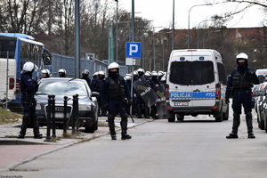 Policjanci w hełmach zabezpieczający mecz piłki nożnej, policyjny radiowóz.