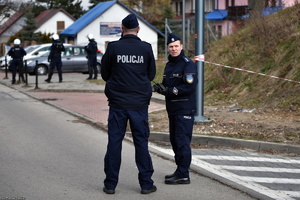 Dwaj umundurowani policjanci rozmawiają ze sobą w tle widoczni inni policjanci.