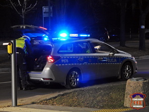 Policyjny radiowóz, policjant zabiera coś z bagażnika.