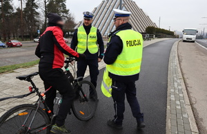 Policjanci z drogówki z żółtych kamizelkach rozmawiają z rowerzystą.