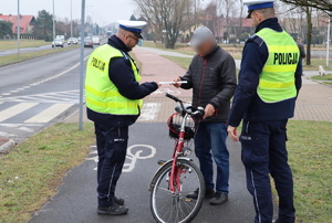 Jeden z policjantów daje rowerzyście opaskę odblaskową, drugi stoi obok.