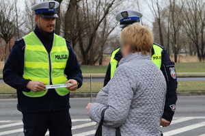 Policjanci z drogówki rozmawiają z kobieta, jedne z nich trzyma opaskę odblaskową.