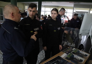 Umundurowany policjant rozmawia z młodzieżą podczas &quot;Dnia Otwartego&quot; w szkole.