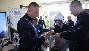 Policjanci pomagają założyć kamizelkę i hełm.