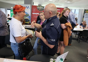 Umundurowany policjant rozmawia z kobietą, widoczne inne osoby.