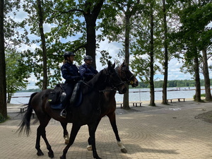 Dwaj umundurowani policjanci patrolują park w tle widoczna woda.