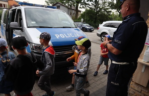 Widoczny radiowóz, do którego idą przedszkolaki, obok stoi policjant.