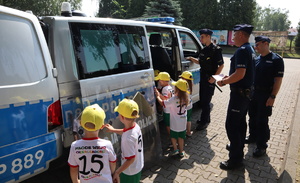 Dzieci wchodzą do policyjnego radiowozu, obok stoi trzech umundurowanych policjantów.