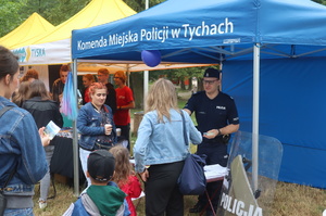 Pod namiotem Komendy Miejskiej Policji w Tychach policjant rozmawia z mieszkańcami, rozdaje im ulotki.