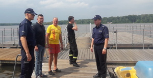 Na zdjęciu widoczni umundurowani policjanci, strażak, i ratownicy. Stoją na molo przy jeziorze.