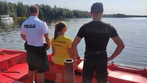 Zdjęcie przedstawiające policjanta, ratownika Wodnego Ochotniczego Pogotowia Ratunkowego oraz strażaka, którzy patrzą na jezioro.