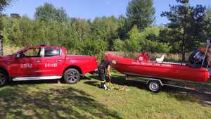 Zdjęcie przedstawiające strażaka, wóz oraz łódź Straży Pożarnej.