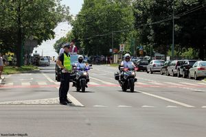 zdjęcie funkcjonariuszy Policji na motocyklach przed samochodem, na którym stoi Biskup święcący pojazdy oraz policjant zabezpieczjący ruch na skrzyżowaniu