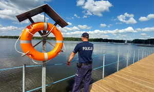Umundurowany policjant stoi na molo przy kole ratunkowym, patrzy w stronę jeziora.