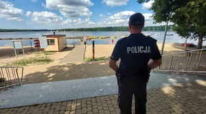Widoczny na zdjęciu policjant stoi tyłem do zdjęcia, zwrócony jest w stronę jeziora.