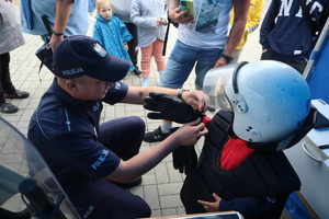 Policjant zakłada rękawiczkę chłopakowi, który przebrał się w strój do zabezpieczania meczy z kamizelka i hełmem.