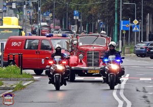 Policjanci na motocyklach za nimi przejazd wozów strażackich.