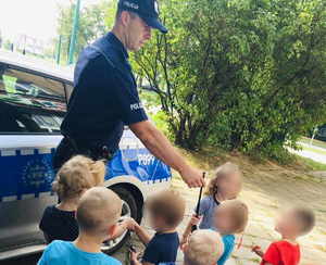 Policjant prezentuje dzieciom sprzęt wykorzystywany w służbie.