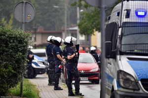 Policjanci w strojach do policyjnego zabezpieczenia meczu, widoczny radiowóz.