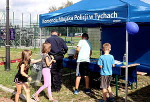 Dzieci oraz umundurowany policjant przy stoisku profilaktycznym Komendy Miejskiej Policji w Tychach.