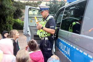 Policjant wydziału ruchu drogowego prezentuje dzieciom latarkę.