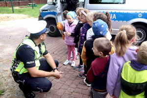 Policjant w wydziale ruchu drogowego kuca przy dzieciach i rozmawia z nimi.