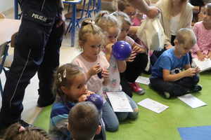 Dzieci siedzą na dywanie, dmuchają balony.