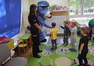 Dzieci witają się z policyjną maskotką &quot;Sznukpiem&quot; i podają mu rękę, obok stoi umundurowana policjantka.