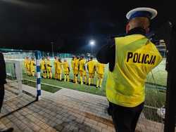 Policjant w odblaskowej kamizelce na boisku z drużyną młodych piłkarzy w odblaskowych strojach.