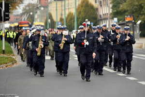 Policjanci policyjnej orkiestry grają na instrumentach, idą w przemarszu ulicą.