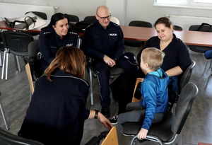 Policjanci wraz z chłopcem i jego mama siedzią na krzesłach i rozmawiają.