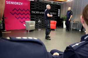Dwaj funkcjonariusze Straży Miejskiej podczas wykładu na konferencji, na pierwszym planie zamazane pagony policjantów.