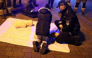 Na zdjęciu umundurowana policjantka i dziecko, które pochyla się przy fantomie do udzielania pierwszej pomocy.