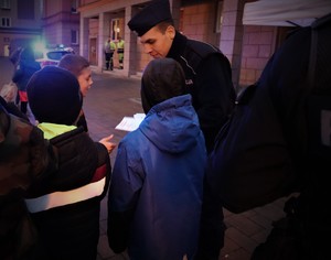 Na zdjęciu umundurowany policjant rozdający dzieciom Elementarze Bezpieczeństwa.