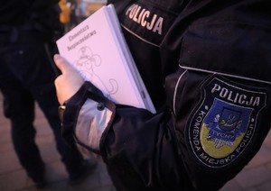Policjant w mundurze trzymający Elementarze Bezpieczeństwa. Na naszywce rękawa napis  POLICJA Komenda Miejska Policji Tychy.