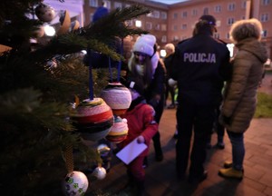 Na zdjęciu choinka z bombkami oraz umundurowana policjantka z kobietą stojące tyłem.