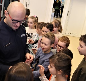 Na zdjęciu grupa dzieci stojąca przy umundurowanym policjancie.