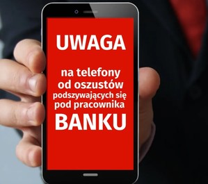 Na zdjęciu telefon komórkowy trzymany w ręce. Na wyświetlaczu telefonu napis: Uwaga na telefony od oszustów podszywających się pod pracownika banku.